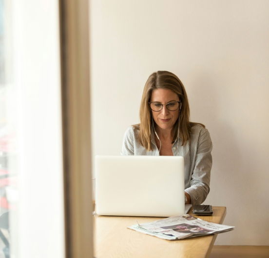 woman wearing grey striped dress shirt sitting down near brown wooden table in front of white laptop computer